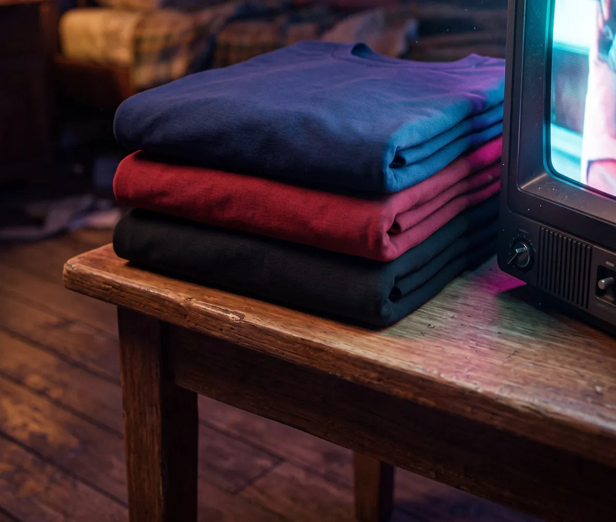 Três camisetas dobradas ao lado da TV de tubo acesa